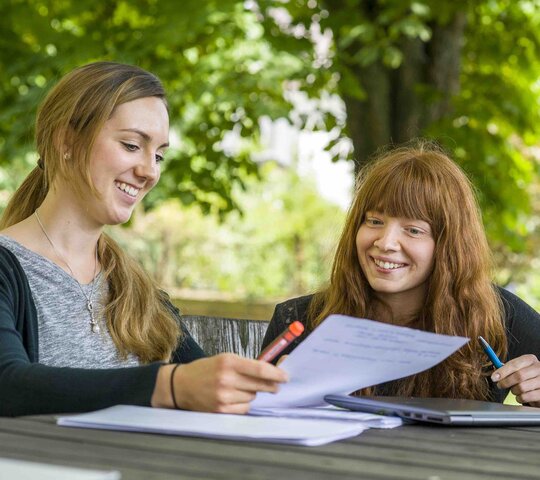 Zwei Studentinnen sitzen im Innenhof des Altbaus der Pädagogischen Hochschule Heidelberg auf Mobiliar, das PHeelGood mitgestaltet hat und ermöglicht so gesundes Studieren. 