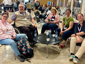 Das Bild zeigt eine Gruppe von Teammitgliedern des AW-ZIB auf der Tagung in der Schweiz. Vier Frauen und ein Mannim Rollstuhl sitzen um einen niedrigen Tisch herum und lächeln in die Kamera.