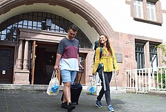 Das Bild zeigt zwei Studierende mit Koffer bzw. Rucksack. Im Hintergrund sieht man den Altbau der Hochschule.