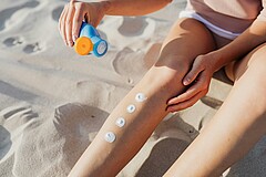 Zwei Beine sind abgebildet mit Sonnencremetupfen darauf und einer Hand, die eine Sonnencremetube hält