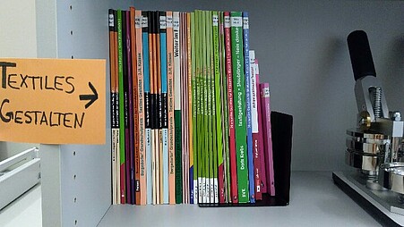 Ein Regalbrett, auf dem sich einige Bücher zum Thema textiles Gestalten befinden.