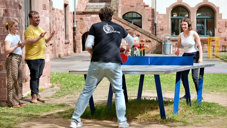 Neben dem Studium gibt es am Campus an der Pädagogischen Hochschule Heidelberg noch viele andere Aktivitäten. Zu sehen sind zwei Menschen beim Tischtennis Spielen. Ein Mann trägt ein T-Shirt mit der Aufschrift "Fachschaft Musik".