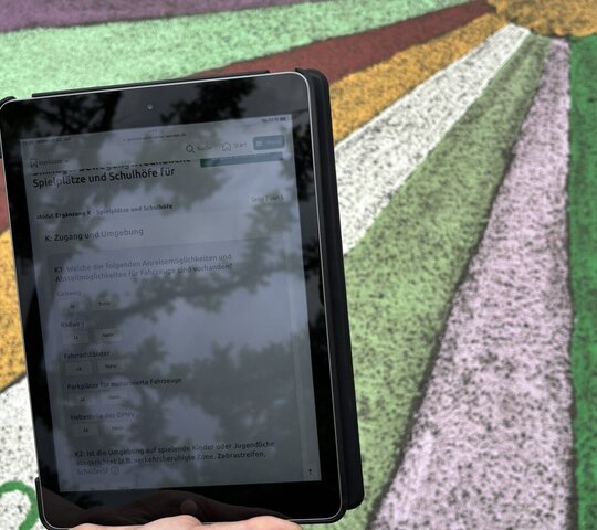 Das Foto zeigt ein Tablet mit dem Fragebogen der Wissenschaftler, im Hintergrund ist ein bemalter Fußboden eines Schulhofs