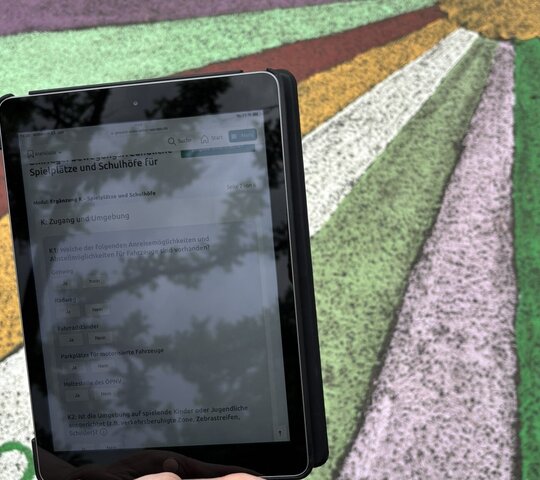 Das Foto zeigt ein Tablet mit dem Fragebogen der Wissenschaftler, im Hintergrund ist ein bemalter Fußboden eines Schulhofs