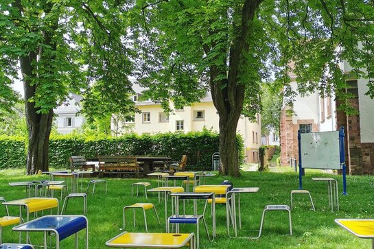 Abgebildet sind Sitz-Tisch-Kombinationen, die im Altbauhof auf der Wiese stehen und von alten Bäumen umgeben sind