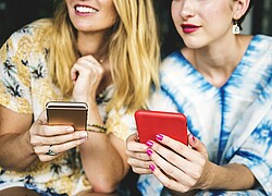 Zwei Frauen mit einem Handy in der Hand.