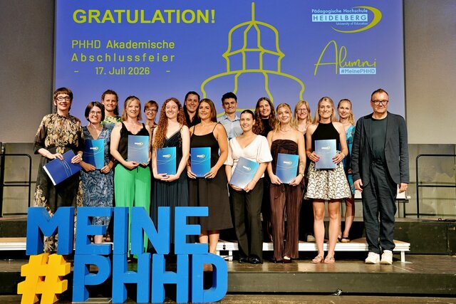 Zu sehen sind Absolvent:innen der PHHD, die sich mit ihren Urkundenmappen auf der Bühne zum Gruppenfoto aufgestellt haben.
