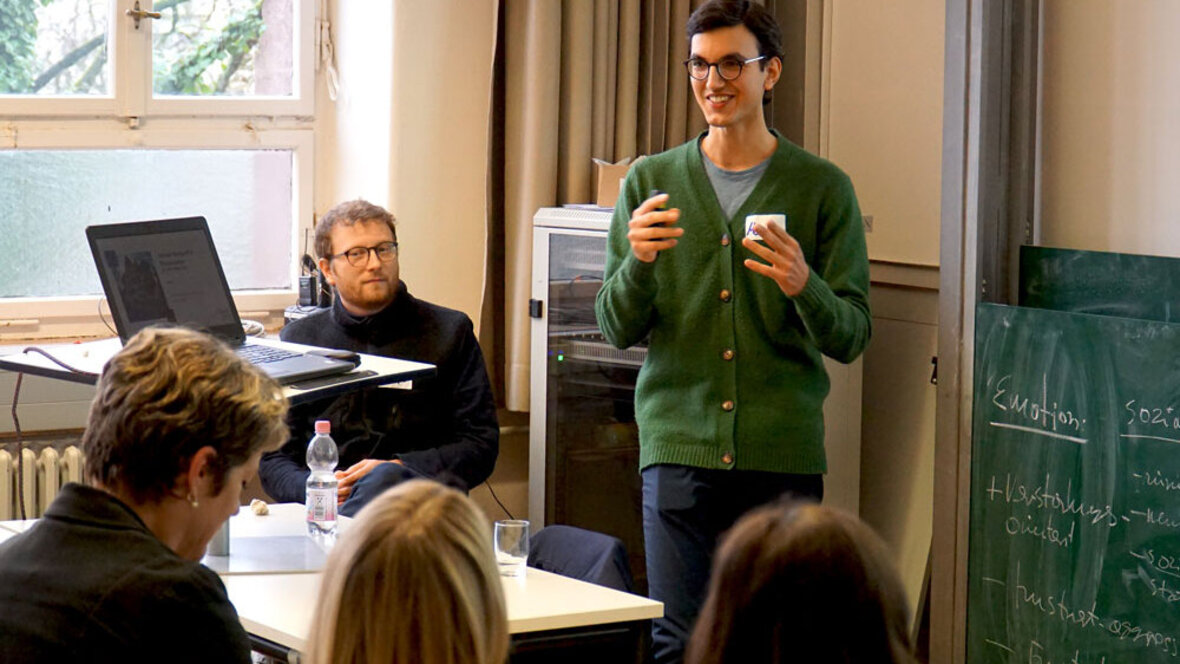 Ein junger Mann steht im vollen Seminarraum und spricht deutlich mit den Händen