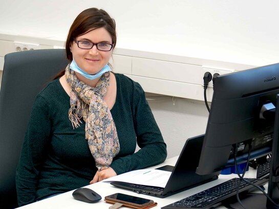 Das Bild zeigt Anna Neff sitzend vor ihrem Arbeitscomputer.