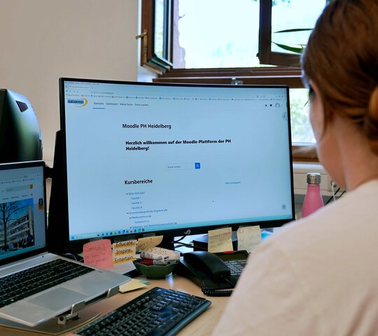 Frau sitz vor PC auf dem man die moodle-Seite der Pädagogischen Hochschule Heidelberg sieht