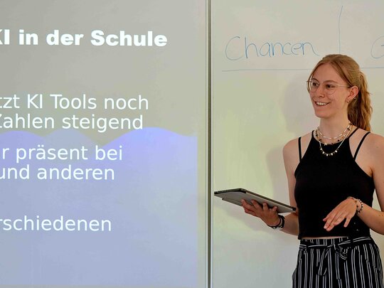 Eine Frau steht vorne im Seminarraum und präsentiert.