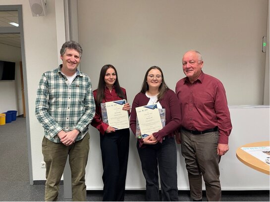 Das Foto zeigt vier Personen in die Kamera lächeln.