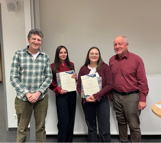 Das Foto zeigt vier Personen in die Kamera lächeln.