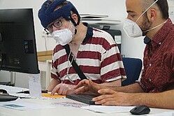Zwei Männer mit Maske vor Computer
