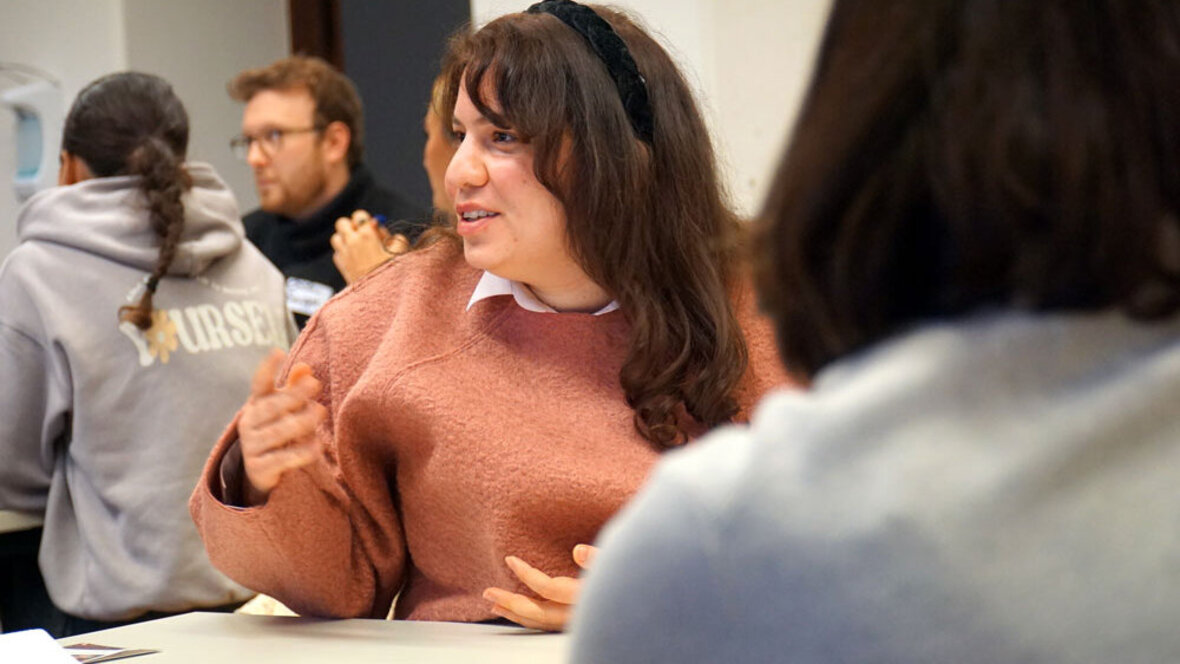 Eine Studentin sitzt in einem Workshop und spricht deutlich mit den Händen.