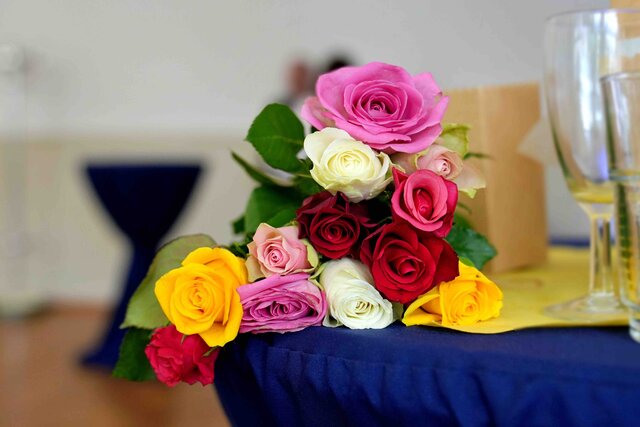 Zu sehen ist ein Strauß bunter Rosen auf einem Stehtisch.