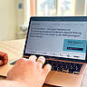 Man sieht primär einen Laptop. Auf diesem ist die Website digiatschool4all.de zu sehen.