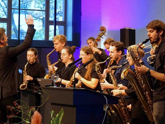 Zu sehen ist ein Orchester mit Dirigenten. 