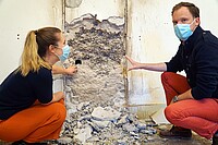 Das Bild zeigt eine Frau und einen Mann, die vor einer teilweise aufgebrochenen Wand knien. Beide tragen aufgrund der Corona-Pandemie Masken. Copyright: Pädagogische Hochschule Heidelberg.