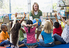 Das Symbolbild zeigt eine junge Frau mit einer Weltkugel in der Hand vor einer Gruppe von Kindern. Foto: clipdealer