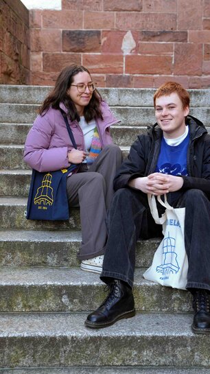 Zu sehen sind zwei Studenten, die auf einer Treppe sitzen.