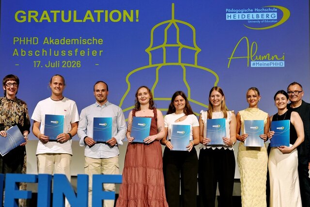 Zu sehen sind Absolvent:innen der PHHD, die sich mit ihren Urkundenmappen auf der Bühne zum Gruppenfoto aufgestellt haben.