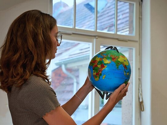 Eine Studentin steht in einem Raum der Pädagogischen Hochschule und sucht auf einem Globus die Länder der internationalen Hochschulpartner der PH.