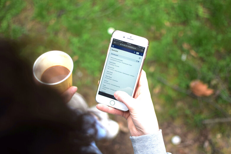 Auf dem Symbolbild hat eine Studentin ein Handy, auf dem man die Stud.IP-Plattform der Hochschule sieht, und einen Kaffee in der Hand. Copyright: Pädagogische Hochschule Heidelberg