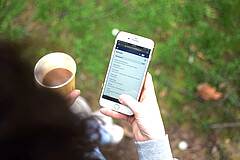 Auf dem Symbolbild hat eine Studentin ein Handy, auf dem man die Stud.IP-Plattform der Hochschule sieht, und einen Kaffee in der Hand. Copyright: Pädagogische Hochschule Heidelberg