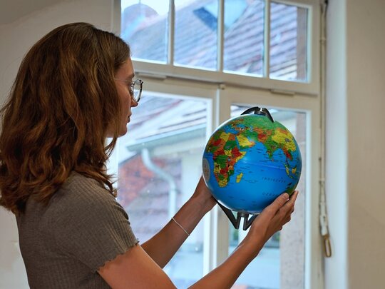 Eine Studentin steht in einem Raum der Pädagogischen Hochschule und sucht auf einem Globus die Länder der internationalen Hochschulpartner der PH.