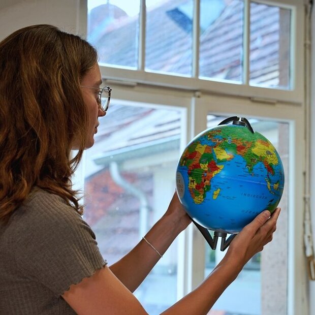 Eine Studentin steht in einem Raum der Pädagogischen Hochschule und sucht auf einem Globus die Länder der internationalen Hochschulpartner der PH.