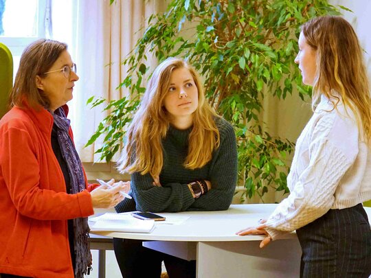 Eine erfahrene Studienberaterin und eine studentische Turorin der Pädagogischen Hochschule Heidelberg beraten eine Studentin. Sie stehen an einem Stehtisch im SSC.