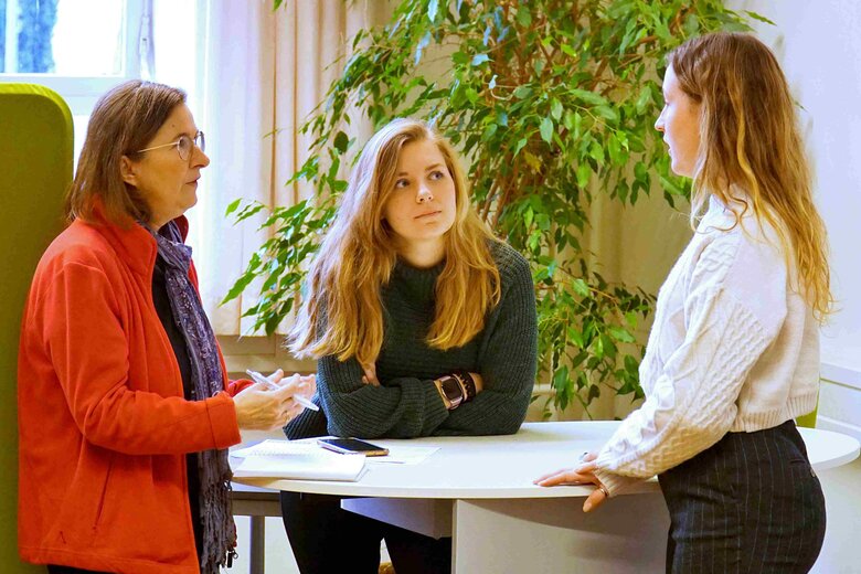 Eine erfahrene Studienberaterin und eine studentische Turorin der Pädagogischen Hochschule Heidelberg beraten eine Studentin. Sie stehen an einem Stehtisch im SSC.