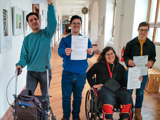 Gruppenaufnahme der Qualifizierungsteilnehmenden nach bestandener Modulprüfung auf dem Flur des Altbaus der Pädagogischen Hochschule Heidelberg. Jede:r hält ein Zertifikat über die bestandene Prüfung in der Hand