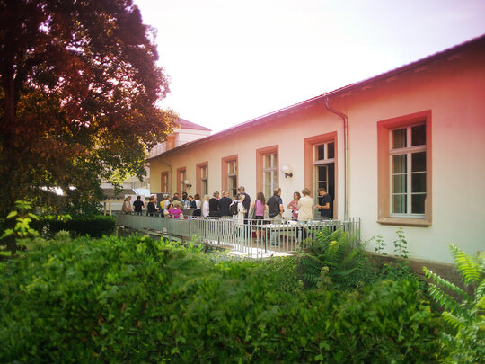 Das Bild zeigt viele Menschen im Gespräch auf der HSE-Terrasse im Abendrot, umgeben von Baum und Büschen.