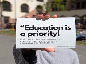 Zu sehen ist eine Person, die auf dem Innenhof der PH Heidelberg einen Flyer des Festival Contre Le Racisme in die Kamera hält.