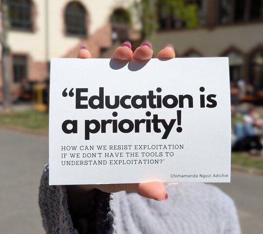 Zu sehen ist eine Person, die auf dem Innenhof der PH Heidelberg einen Flyer des Festival Contre Le Racisme in die Kamera hält.