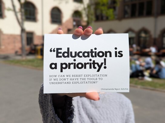 Zu sehen ist eine Person, die auf dem Innenhof der PH Heidelberg einen Flyer des Festival Contre Le Racisme in die Kamera hält.