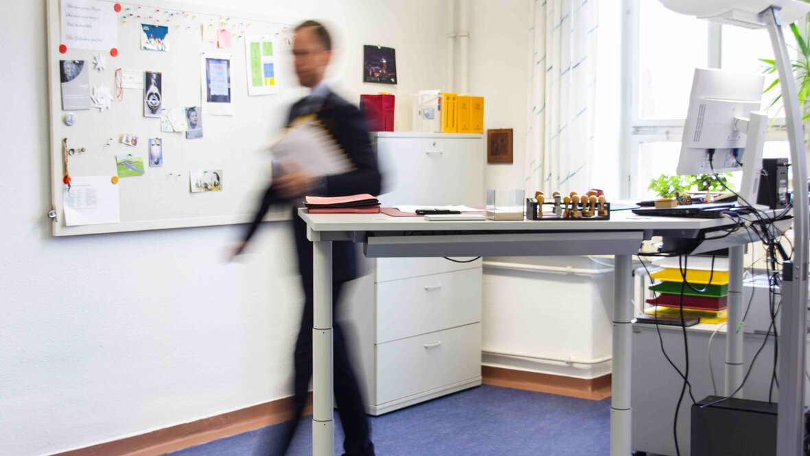 Arbeiten an der PHHD: Eine Person läuft hinter einem höhenverstellbaren Steh-Schreibtisch entlang.