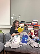 Das Bild zeigt eine Frau umgeben von Büchern auf einer Couch.