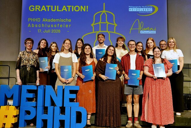Zu sehen sind Absolvent:innen der PHHD, die sich mit ihren Urkundenmappen auf der Bühne zum Gruppenfoto aufgestellt haben.