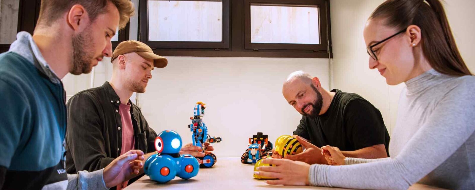 Studierende der Medienbildung sitzen gemeinsam an einem Tisch und erarbeiten sich mit Mediendidaktischem Matieral, Robotern den Lerninhalt.