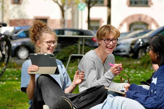 Studierende des Lehramststudium der Pädagogischen Hochschule Heidleberg sitzen im Innenhof der Altbaus auf der Wiese und lachen.