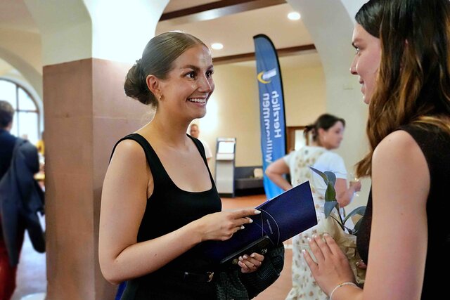 Zu sehen ist eine Alumna, die sich lachend mit einer weiteren Person unterhält.
