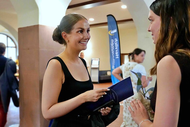 Zu sehen ist eine Alumna, die sich lachend mit einer weiteren Person unterhält.