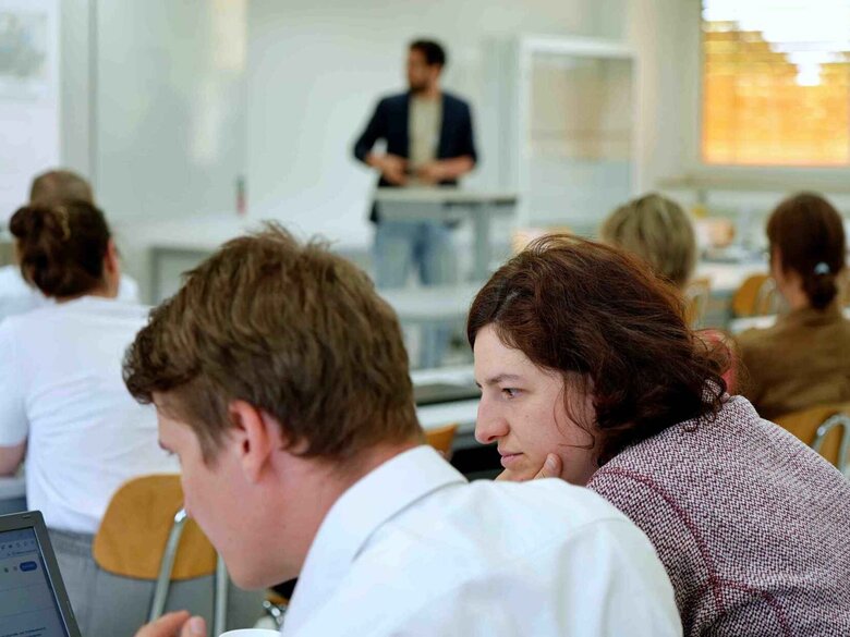 Ein Mann präsentiert vorne im Seminarraum, Studierende machen sich Notizen.