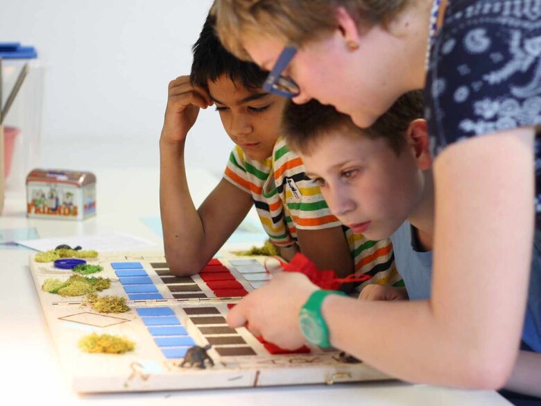 Das Foto zeigt eine Lehrende die zwei Kindern etwas in einem Buch zeigt.