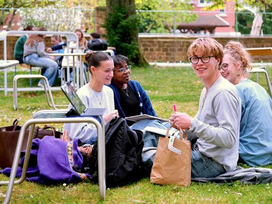 Zu sehen sind Studierende, die auf einer Wiese sitzen.