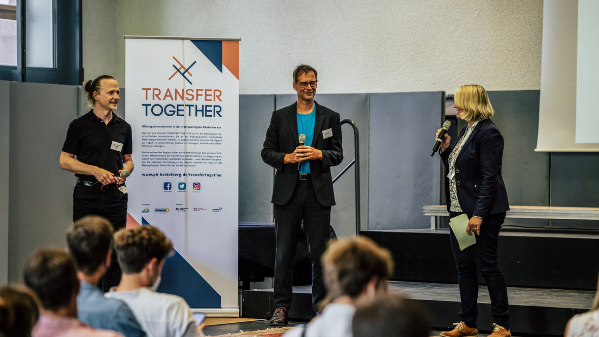 Zu sehen sind Christian Spannagel, Hartmut Lang und Melanie Seidenglanz auf einer Bühne.