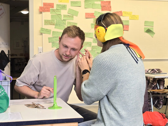 Das Foto zeigt Studierende in einem Seminarraum, die lernen, wie bei Taubblindheit kommuniziert wird. Sie tragen dafür Kopfhörer und eine Augenbinde.